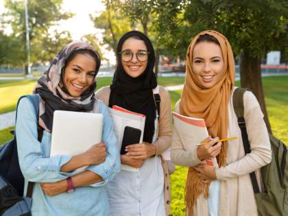 Image of a happy young arabian women students holding books in park outdoors.
