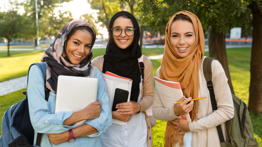 Image of a happy young arabian women students holding books in park outdoors.